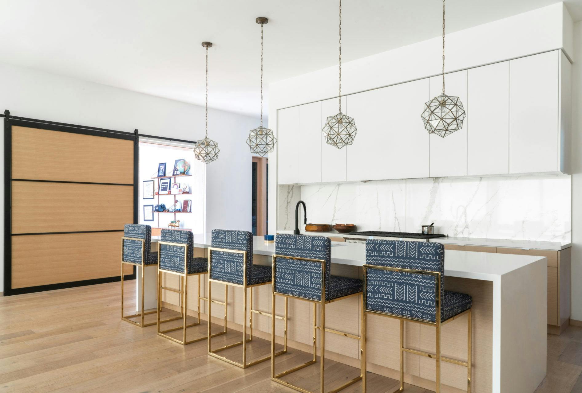 A clean white kitchen accented with patterned counter stools and custom pendants.