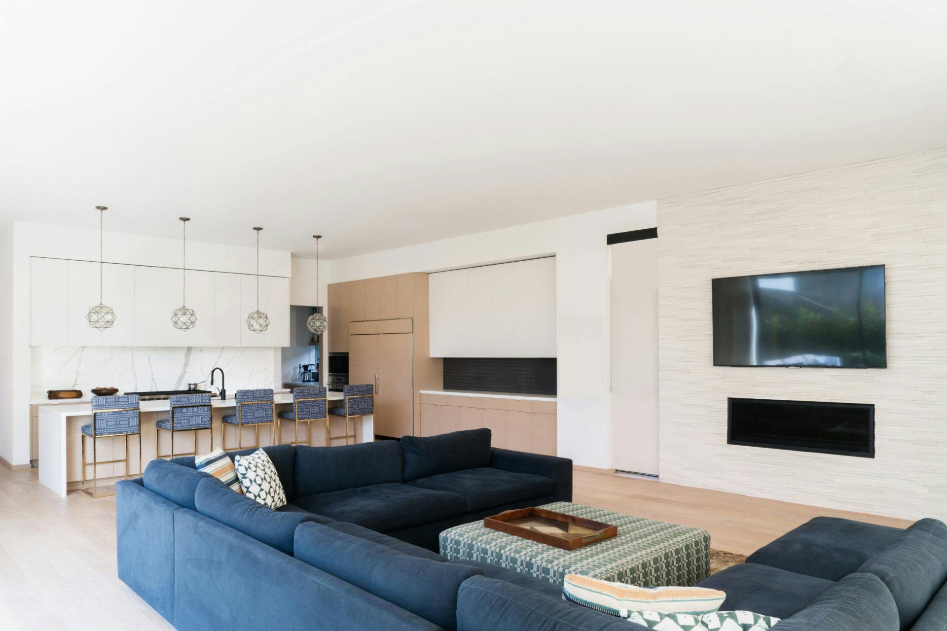 The family room is an extension of the kitchen. Custom 17' dark blue sectional with an ottoman from Amber Interiors and custom brass counter stools.