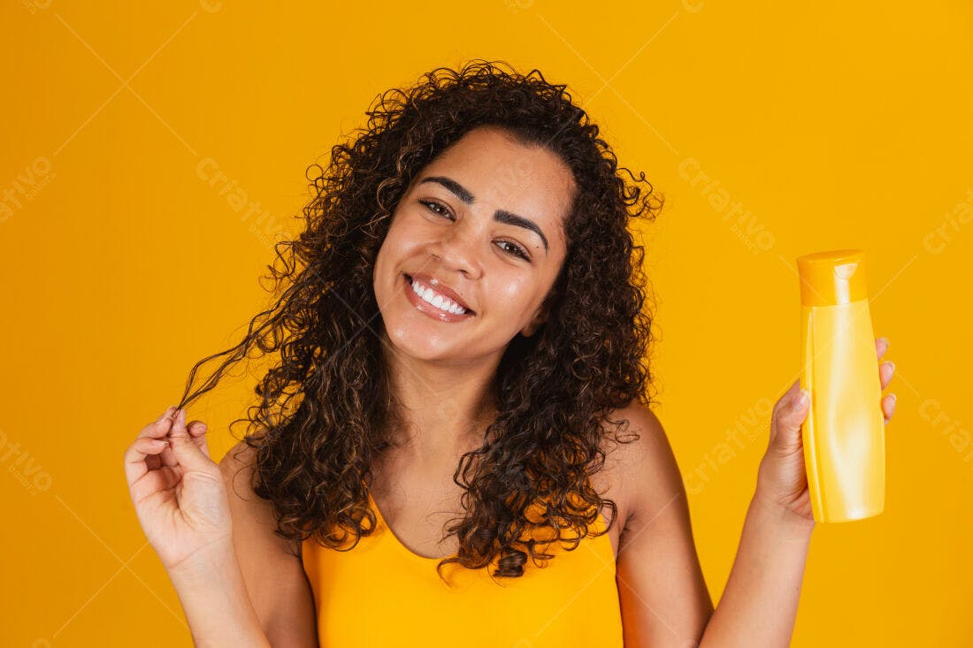 Mulher sorridente com cabelo cacheado segurando shampoo amarelo