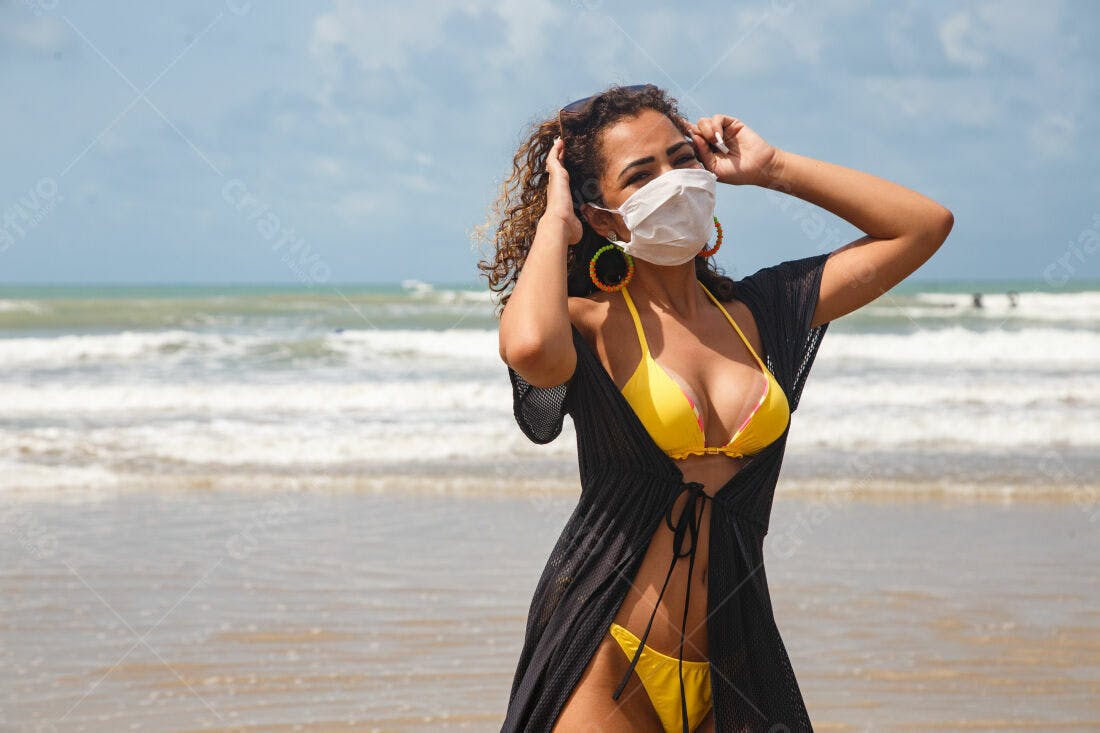 Mulher na praia com máscara e biquini amarelo