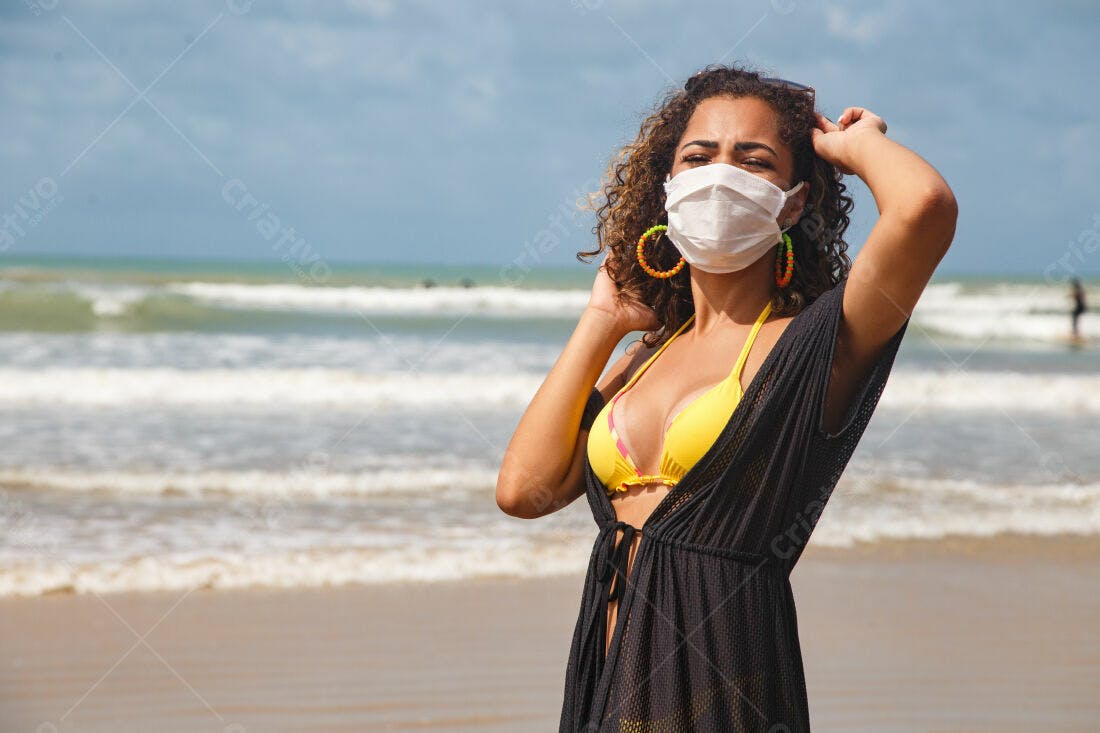 Mulher na praia com máscara usando biquini amarelo