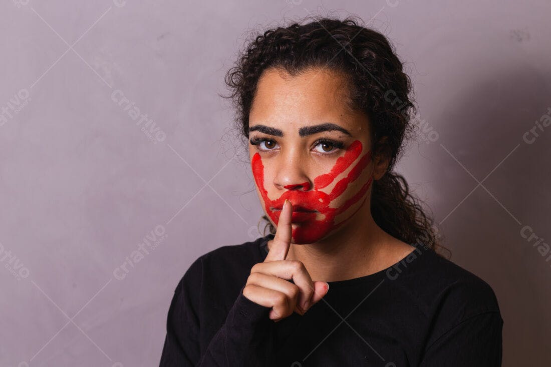 Mulher com pintura vermelha no rosto pedindo silêncio