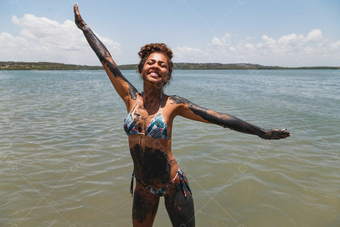 Mulher na praia coberta de lama negra sorrindo