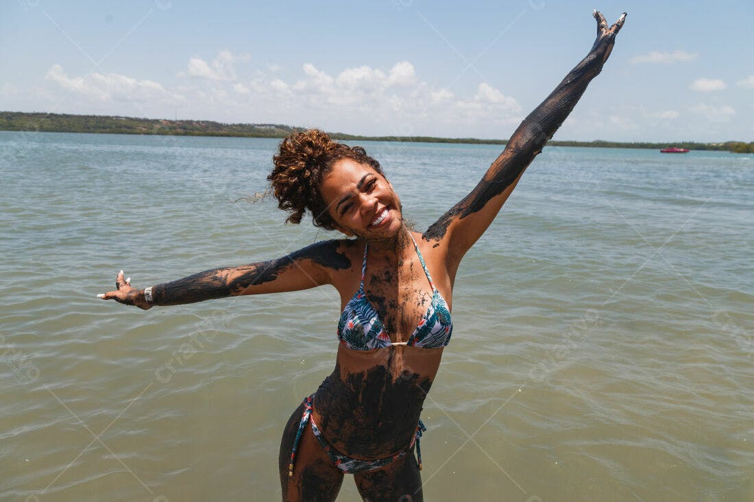 Mulher na praia coberta de lama sorrindo