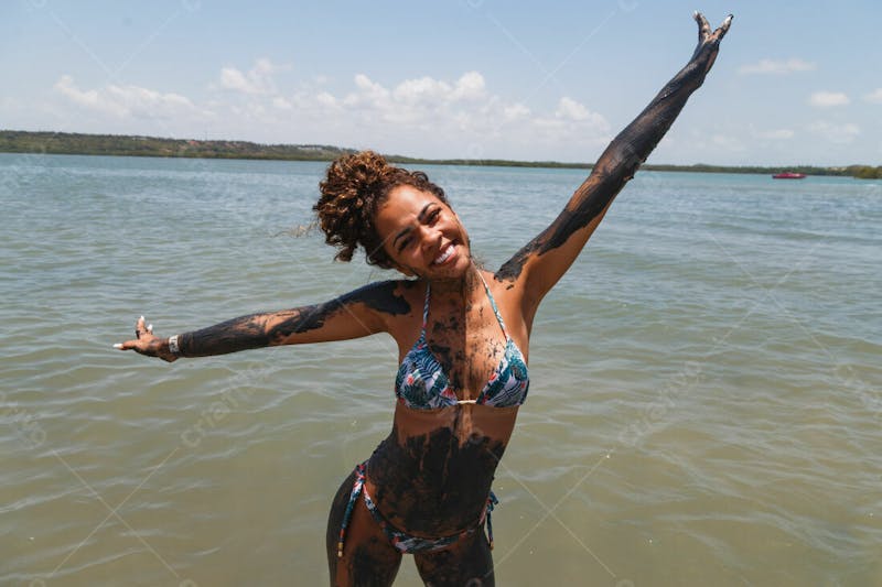 Mulher bonita morena feliz com braços abertos na praia corpo com barro 4