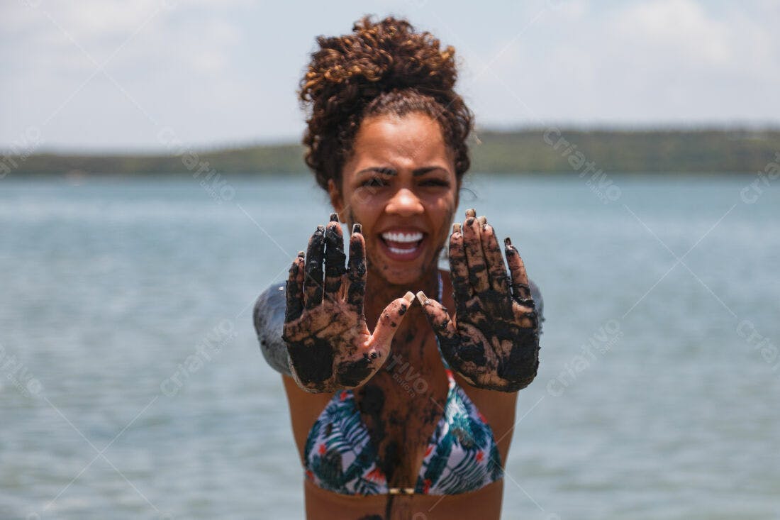 Mulher negra com lama preta nas mãos na praia