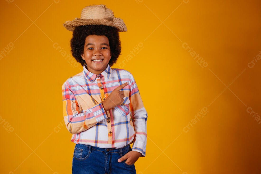 Menino sorridente aponta com chapéu de palha fundo amarelo