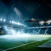 Modernized soccer stadium full of smoke and illuminated by lights