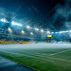 Modernized soccer stadium filled with smoke and illuminated by lights.