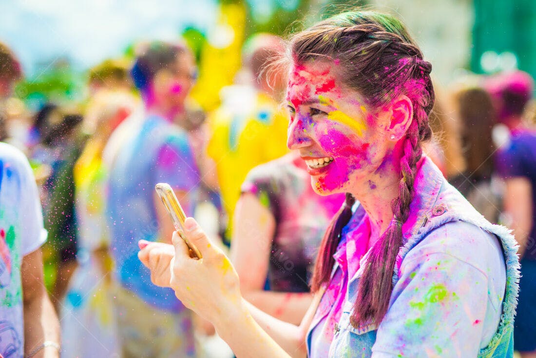 Mulher na Holi usando celular cores vibrantes