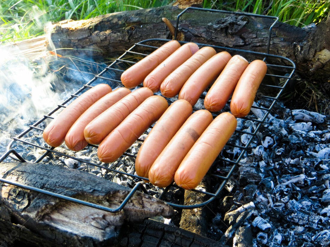 Salsichas grelhando em churrasqueira ao ar livre
