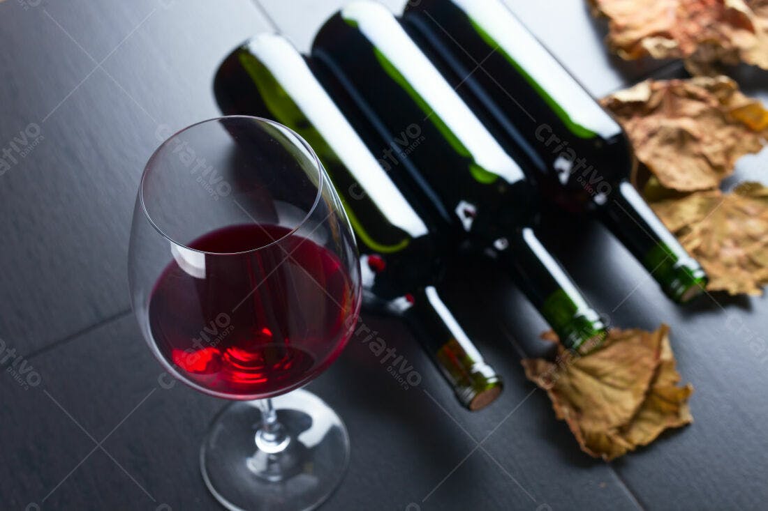 Taça de vinho tinto com garrafas e folhas