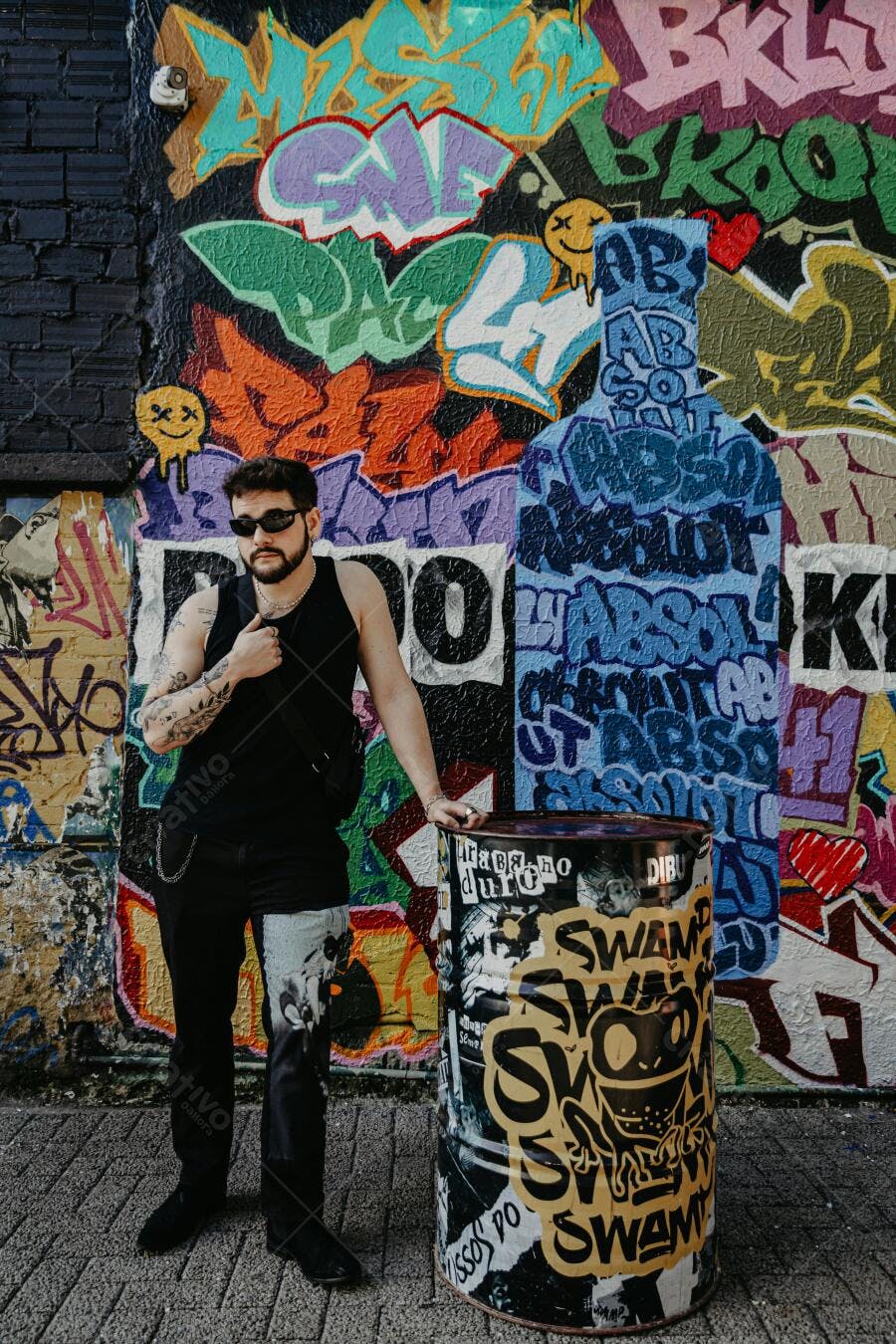 Homem com barba e óculos escuros em frente a grafite colorido