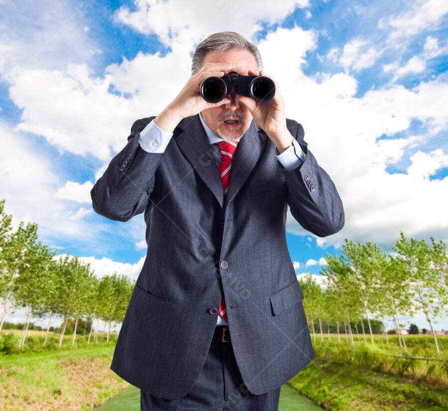 Homem de terno usando binóculos em paisagem verde
