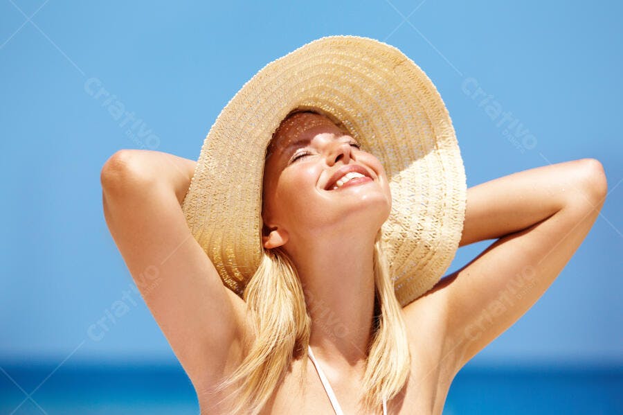 Mulher loira feliz com chapéu de palha na praia