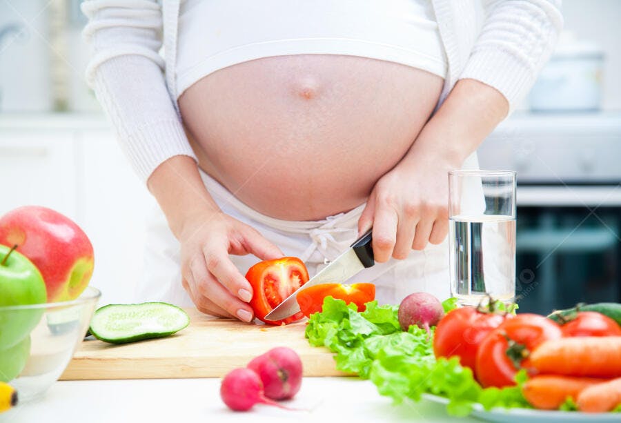 Mulher grávida cortando tomate na cozinha