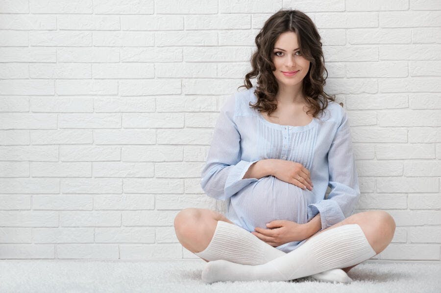 Grávida feliz sentada em chão branco