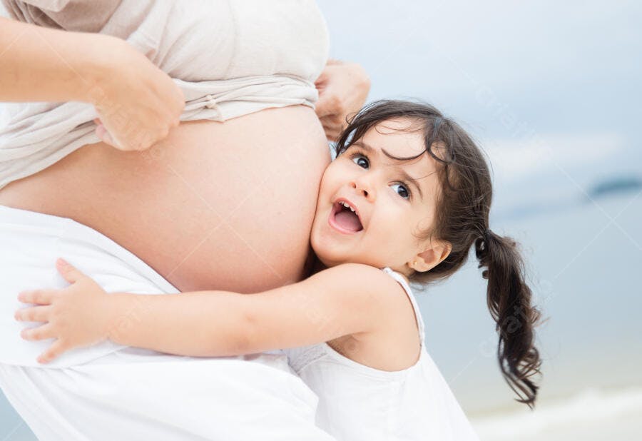 Menina abraçando barriga de grávida na praia