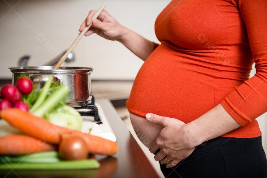 Grávida cozinhando legumes na cozinha
