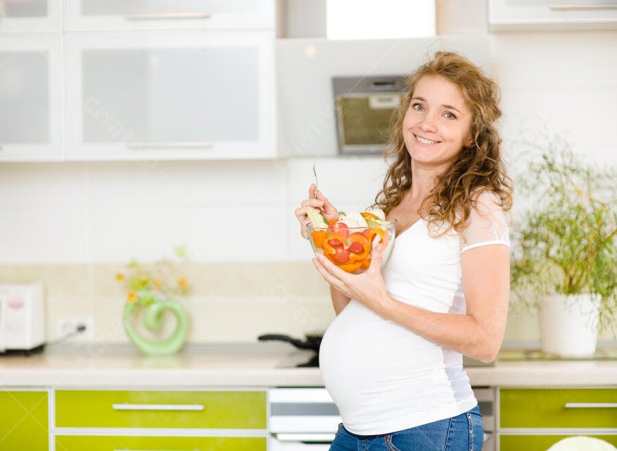 Mulher grávida comendo salada na cozinha