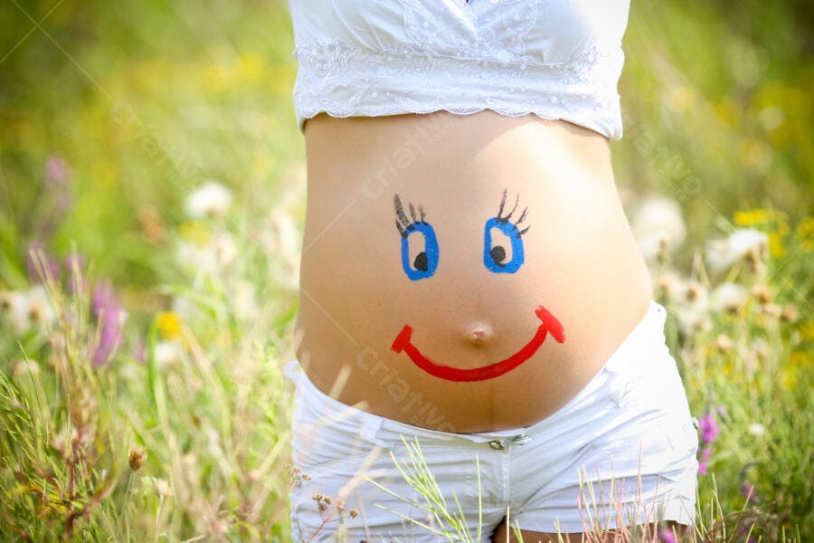 Barriga de grávida com desenho de rosto feliz em campo florido