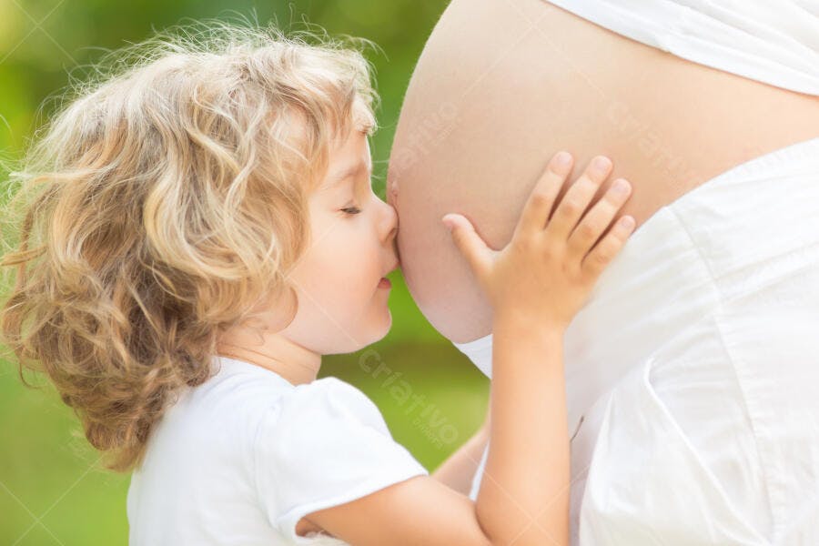Criança beijando barriga grávida ao ar livre