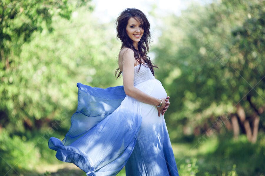 Grávida feliz em vestido azul e branco num jardim