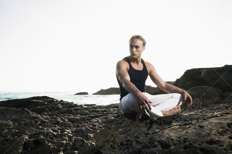 Homem meditando na praia rochas escuras