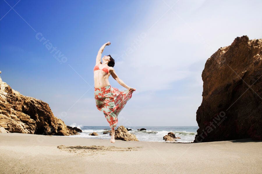 Mulher pulando na praia rochosa