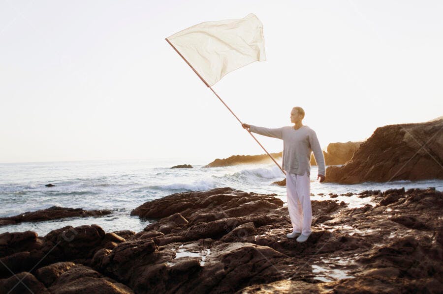 Homem segurando bandeira branca na praia ao entardecer