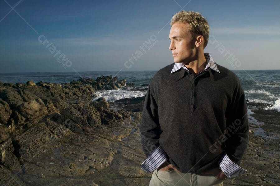 Homem contemplativo na praia rochosa