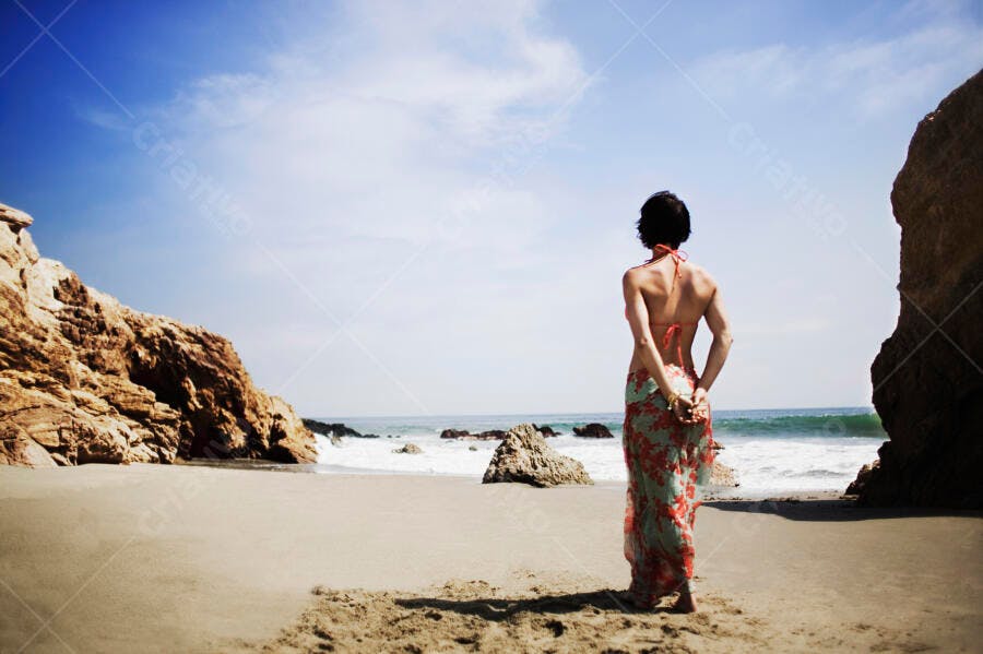 Mulher na praia rochosa contemplando o mar