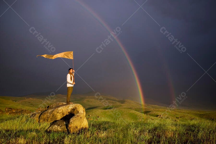 Homem com bandeira em paisagem com arco-íris