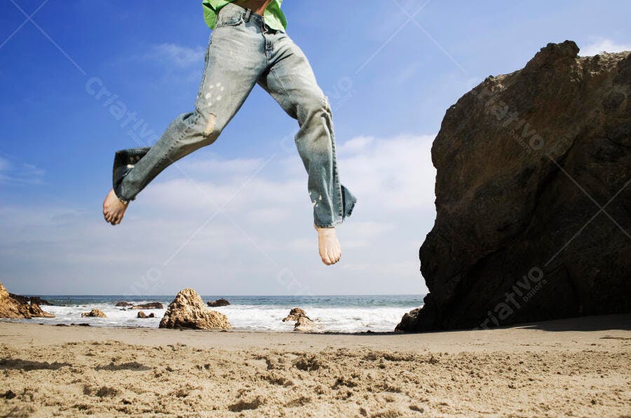 Pernas saltando na praia ensolarada