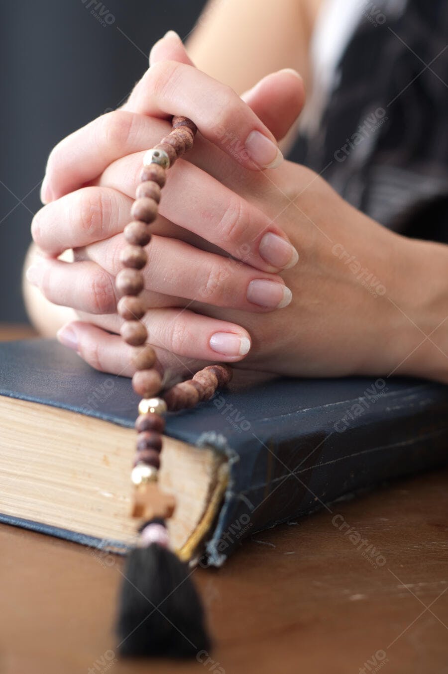 Mãos em oração com terço sobre livro