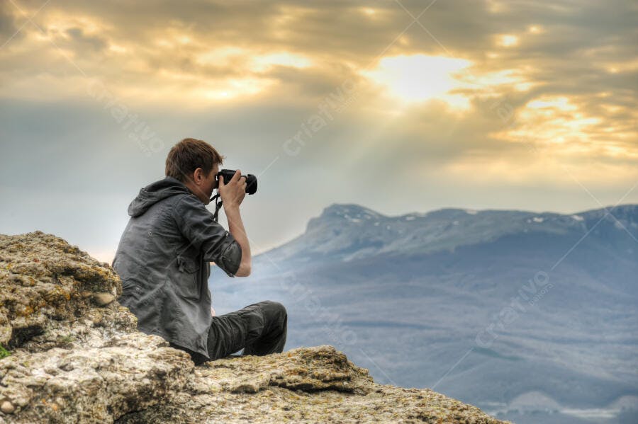 Fotógrafo em penhasco ao pôr do sol