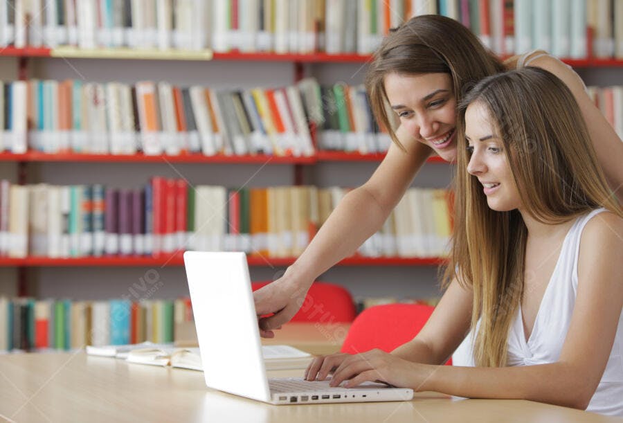 Estudantes universitárias usando laptop na biblioteca