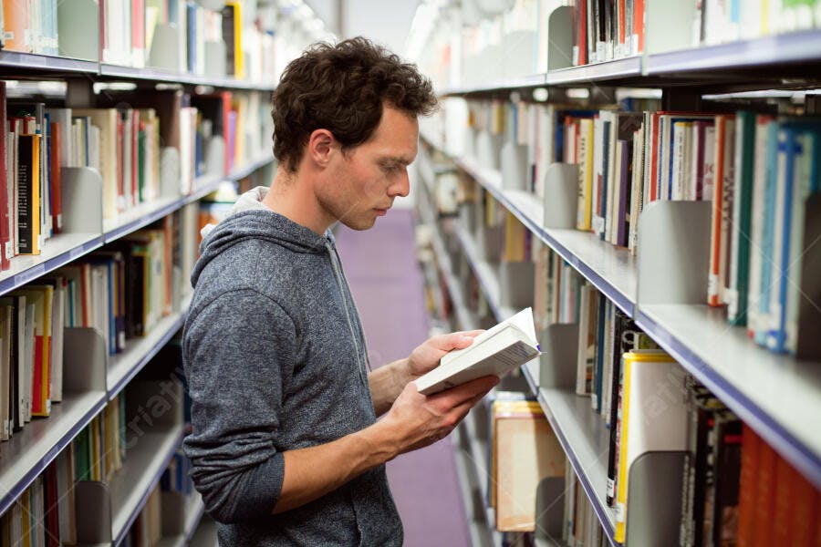 Homem lendo livro em biblioteca universitária