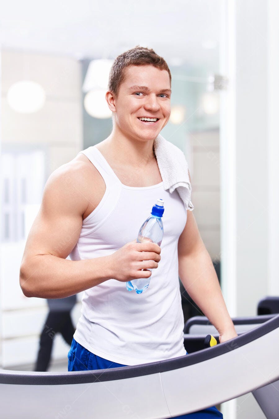 Homem musculoso sorrindo na academia com garrafa de água