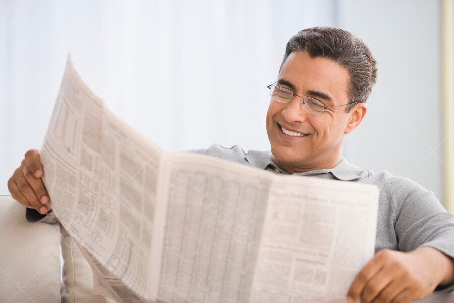 Homem lendo jornal sorrindo em casa