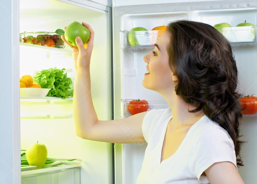 Mulher pegando maçã verde na geladeira