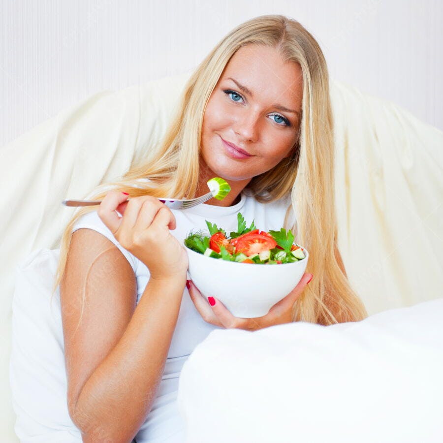 Mulher loira comendo salada fresca na cama