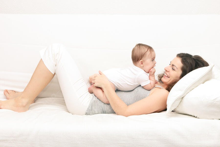Mãe e bebê sorrindo na cama branca