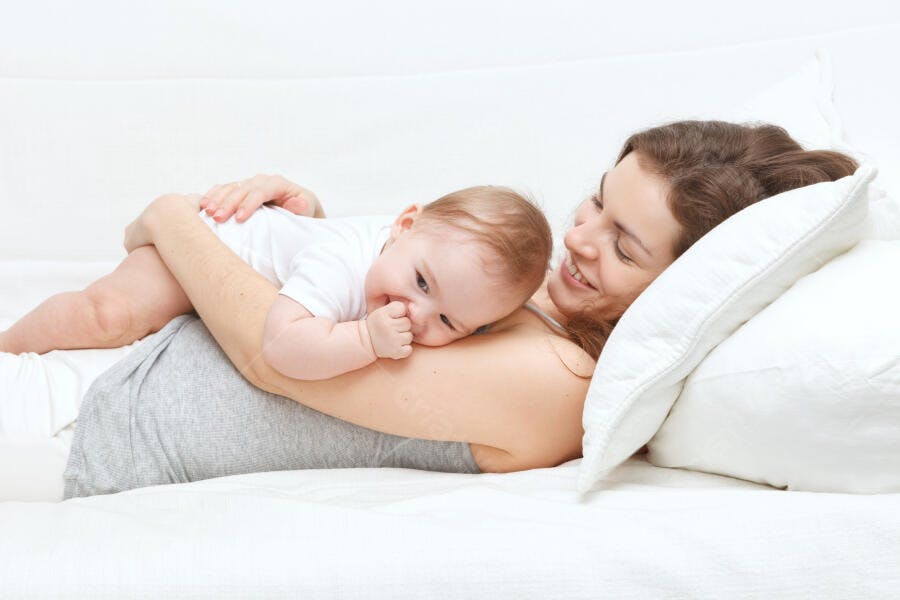 Mãe e bebê sorrindo na cama branca