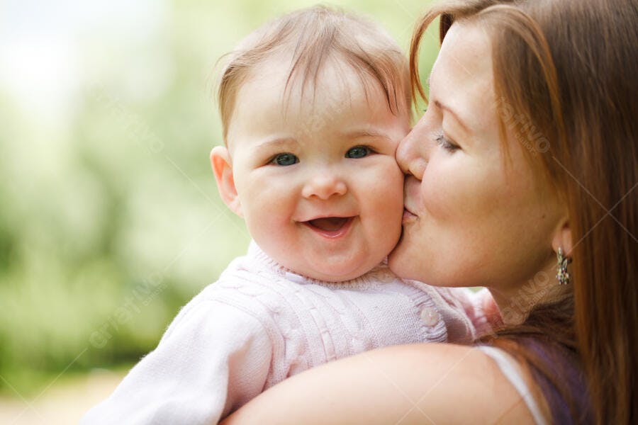 Bebê sorrindo recebendo beijo da mãe ao ar livre
