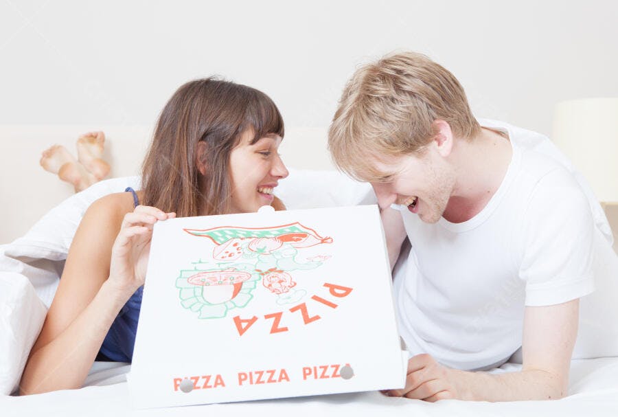 Casal feliz com pizza na cama