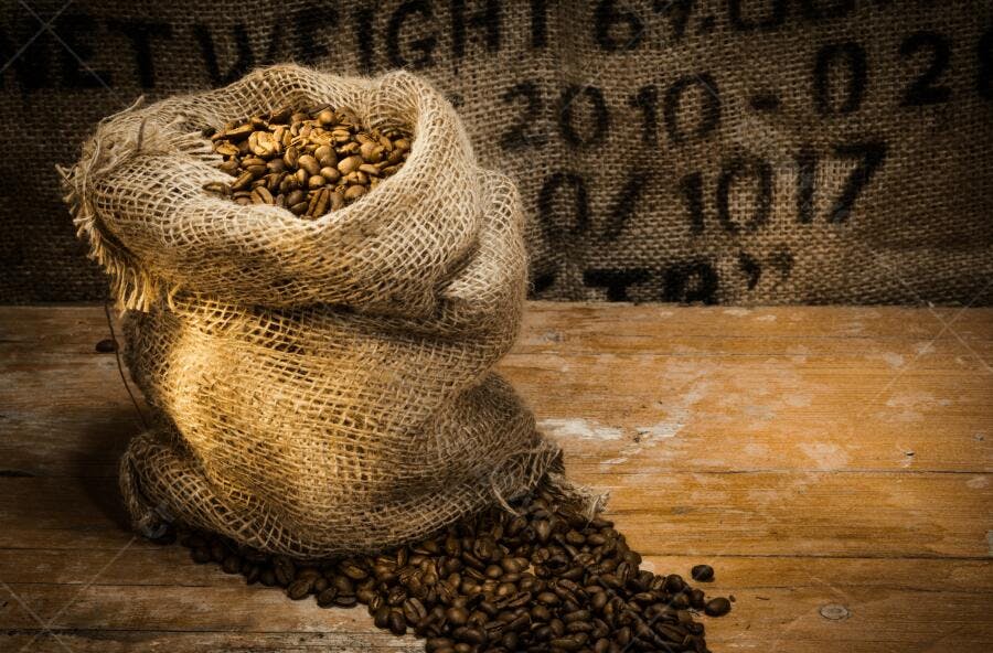Grãos de café em saco de juta sobre madeira