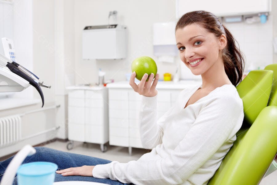 Mulher sorrindo com maçã verde no consultório odontológico