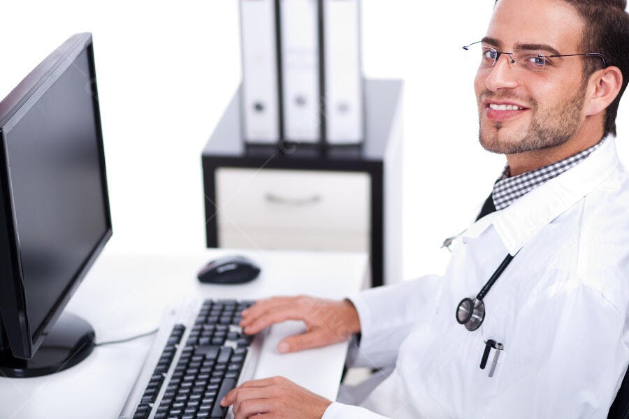 Médico sorrindo usando computador no consultório