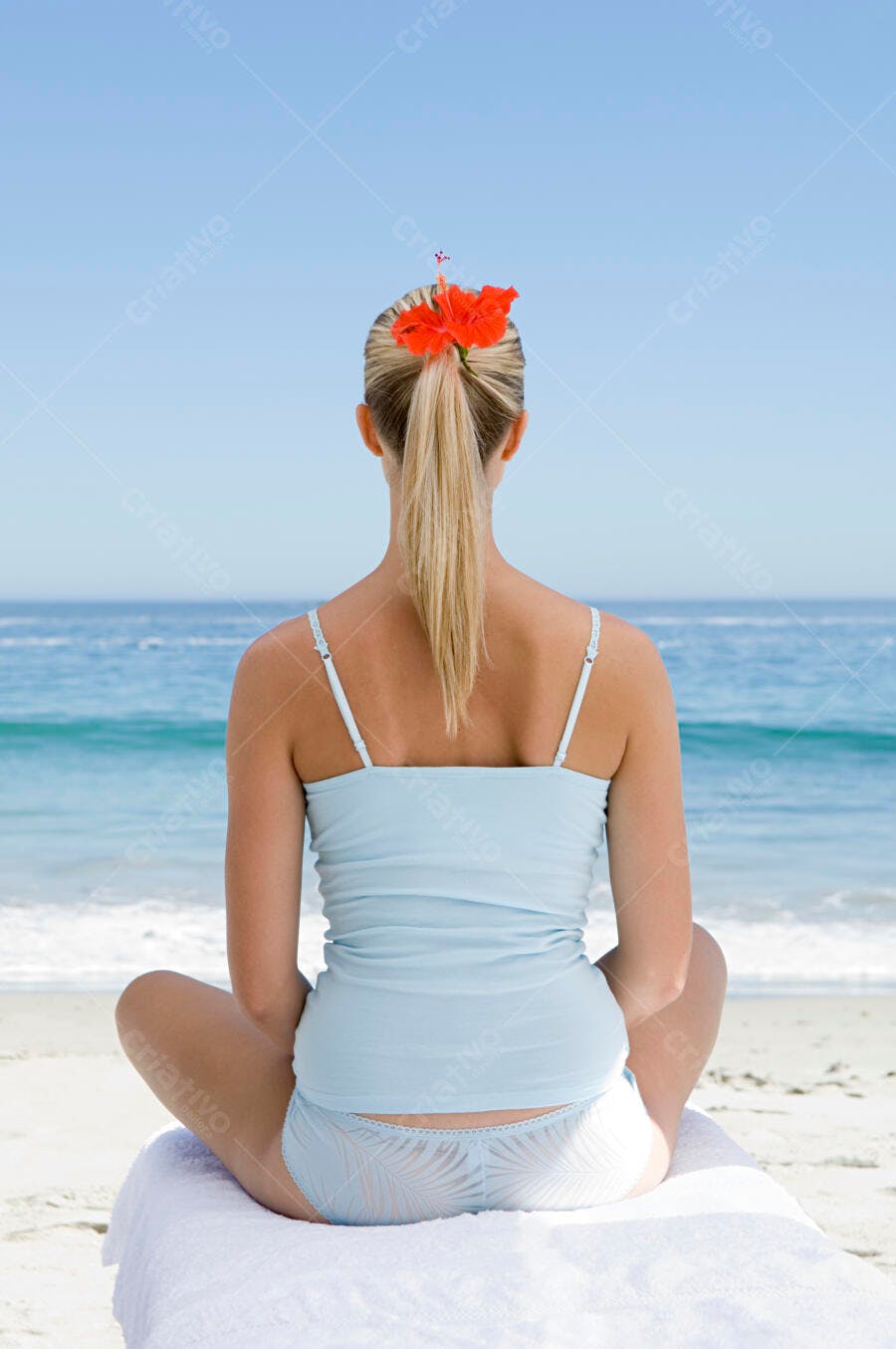 Mulher meditando na praia com flor no cabelo